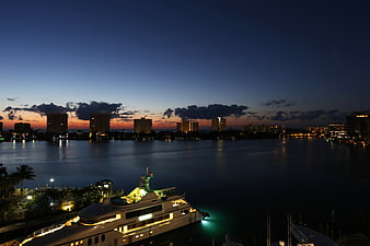 Luxury yacht docked at marina during twilight with city skyline