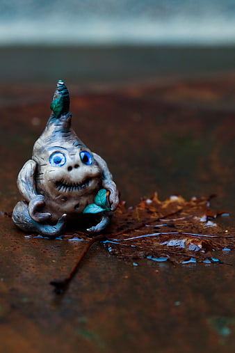 Whimsical clay gnome figurine with blue eyes on wet leaf
