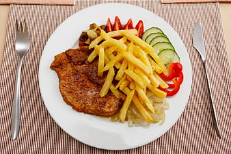Grilled pork steak with french fries and vegetables on white plate