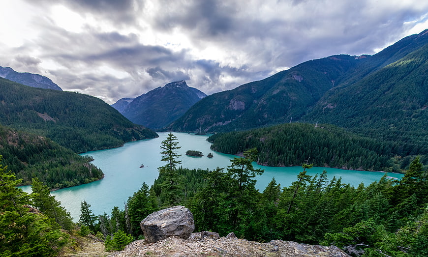 Turquoise glacial lake surrounded by forested mountains under cloudy sky