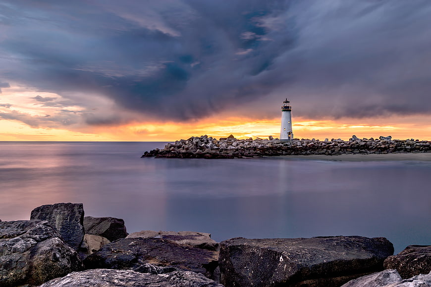 Dramatic Lighthouse on Rocky Jetty at Sunset