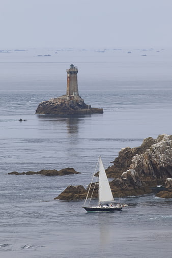 Sailboat passing lighthouse on rocky Brittany coast