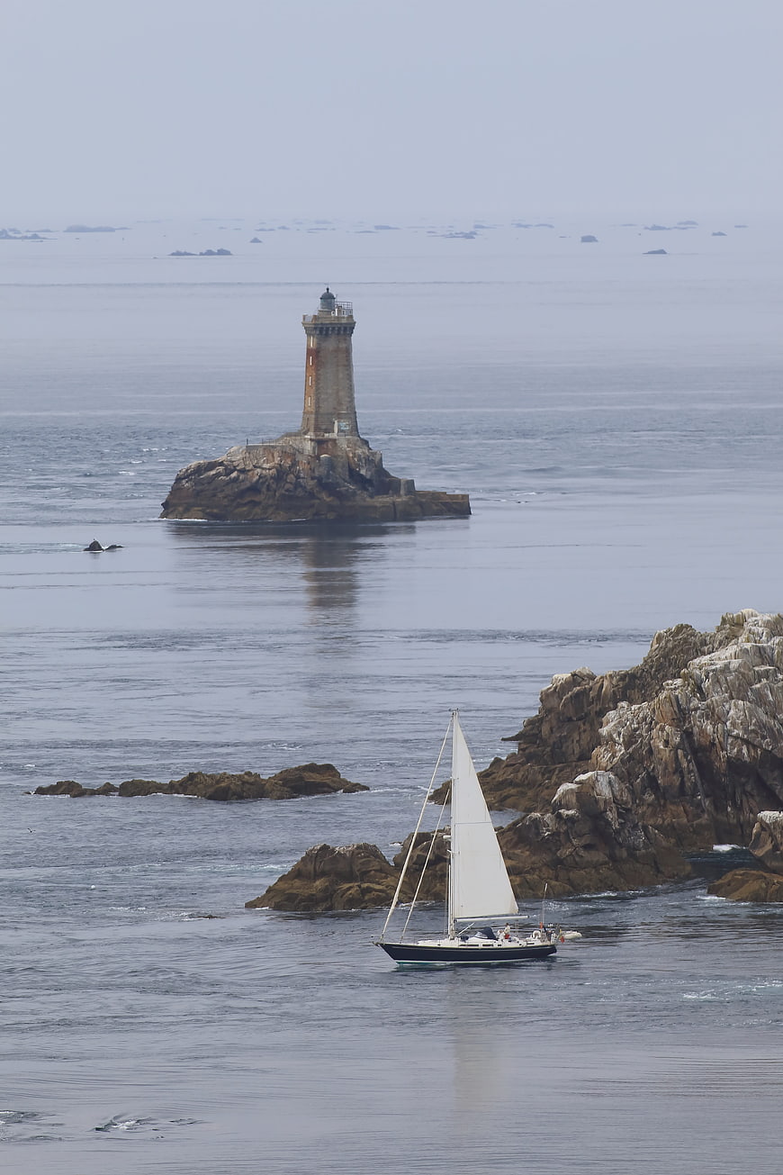 Sailboat passing lighthouse on rocky Brittany coast