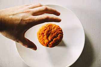 Hand Reaching for Orange Muffin on White Plate