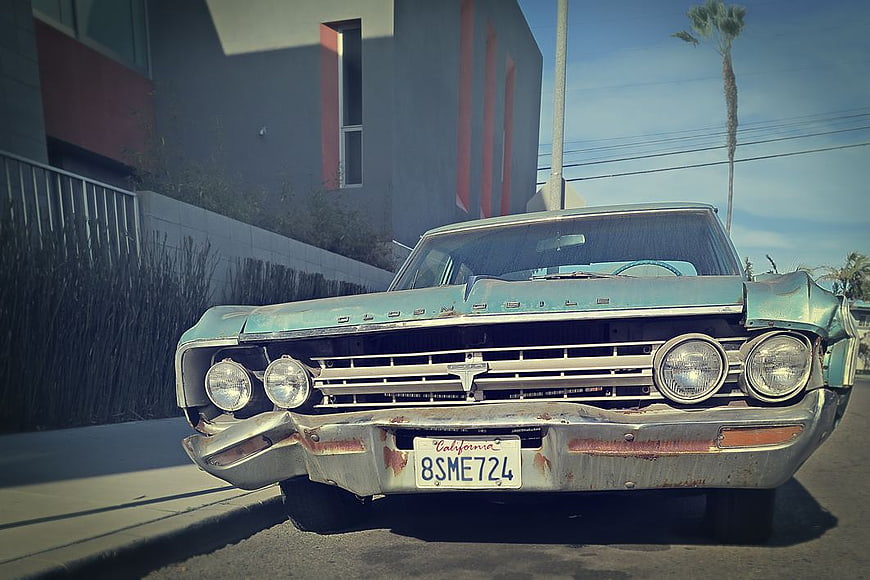 Front view of vintage rusty Oldsmobile parked on street