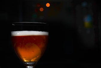 Glass of amber beer with foam in dark pub setting