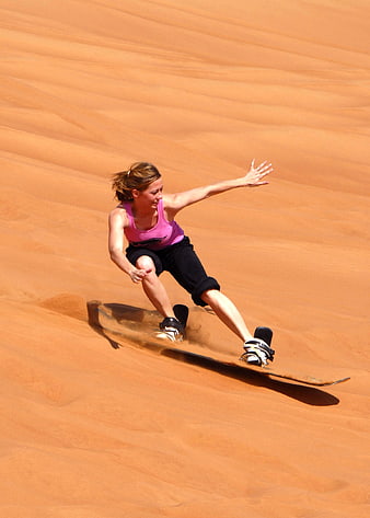 Woman sandboarding down orange desert dune