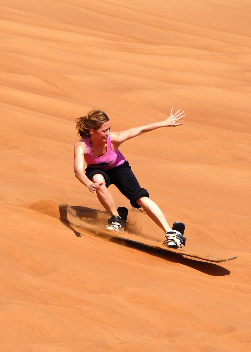 Woman sandboarding down orange desert dune