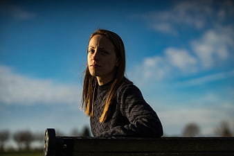 Contemplative Woman Sitting on Park Bench Against Blue Sky