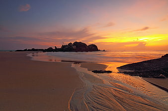 Serene Beach Sunset with Rocky Outcrop and Golden Sky