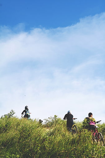 Mountain bikers resting on grassy hilltop under blue sky