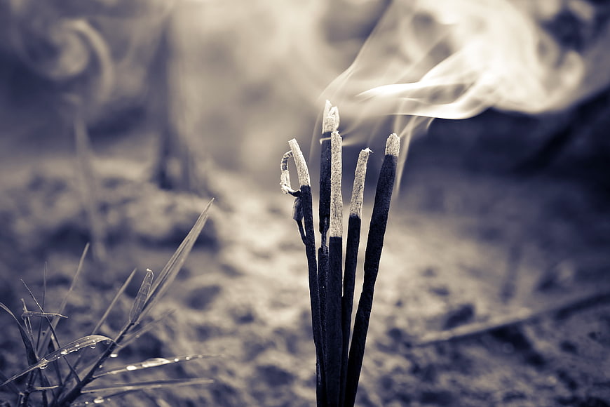 Burning incense sticks with rising smoke in a serene natural setting