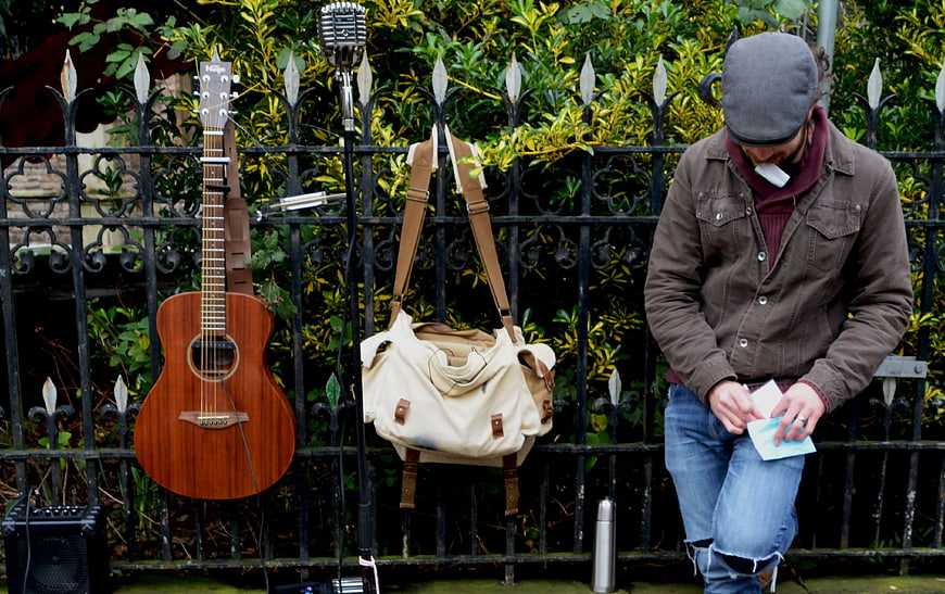 Street musician with guitar and microphone by fence