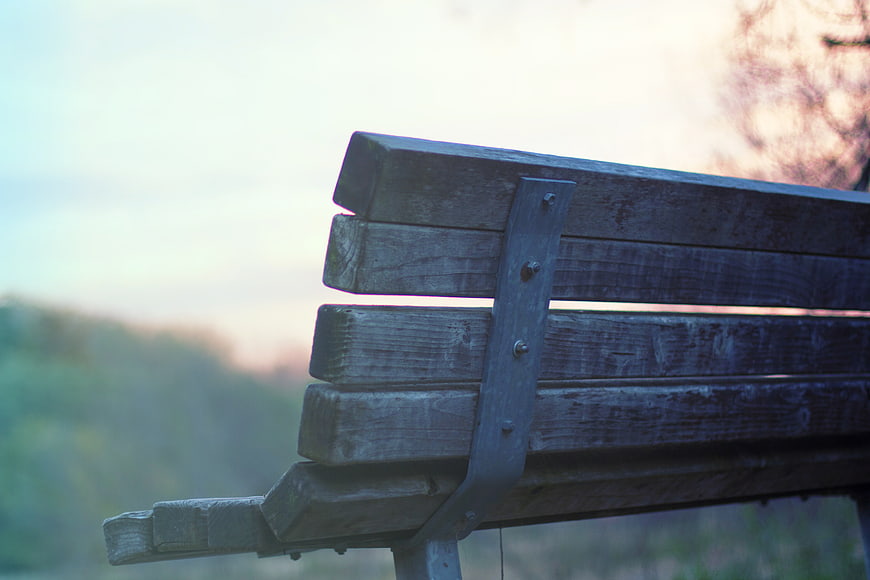 Close-up of weathered wooden park bench against blurred nature background