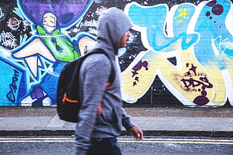 Man in Hoodie Walking Past Colorful Graffiti Wall