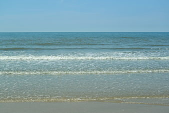 Calm sea waves rolling onto sandy beach horizon