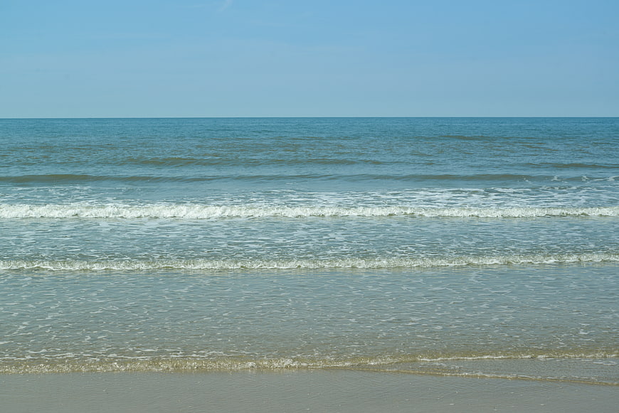 Calm sea waves rolling onto sandy beach horizon