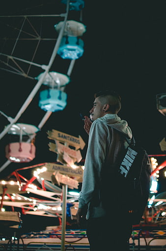 Young man smoking at night with Ferris wheel background