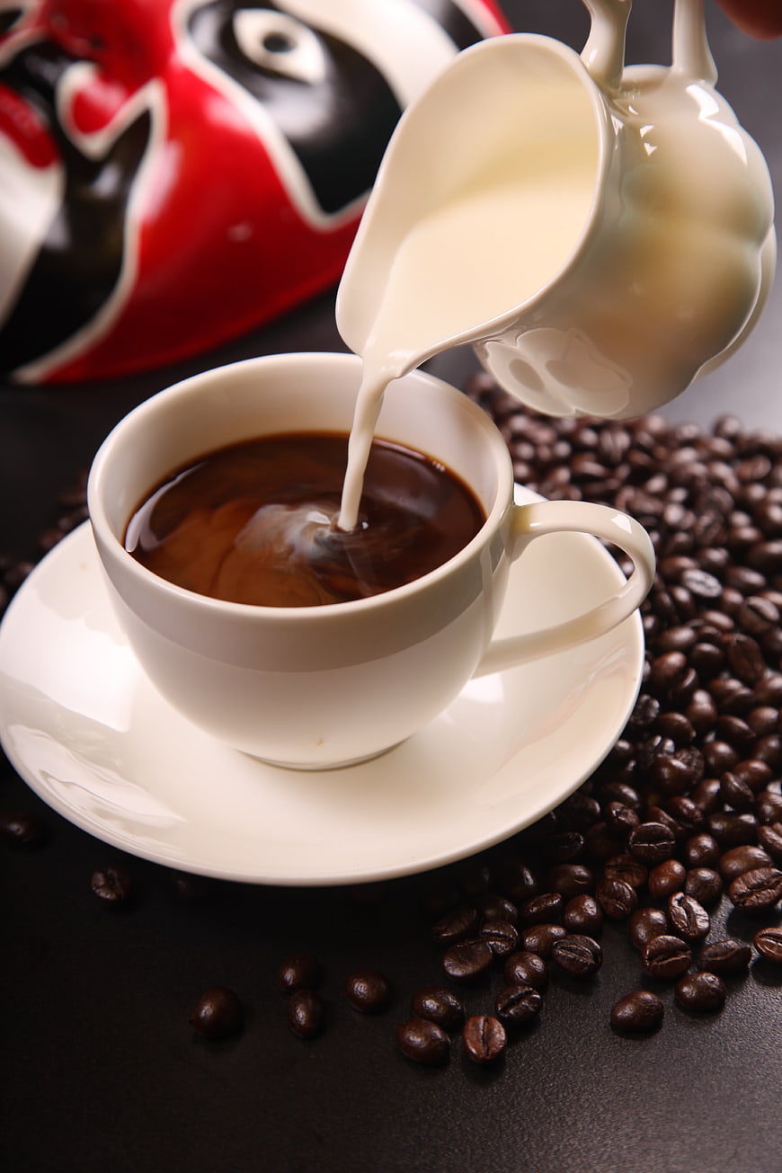 Pouring milk into black coffee cup with beans