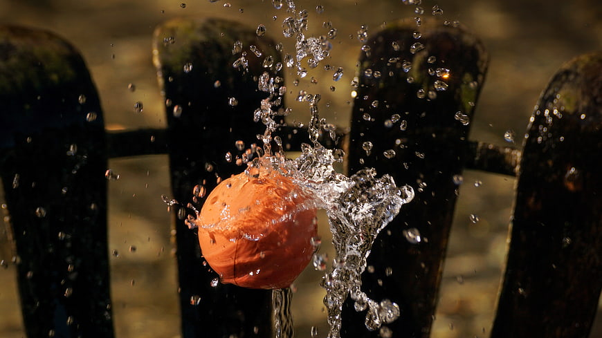 Orange Ball Splashing Water Against Dark Stone Fountain Background