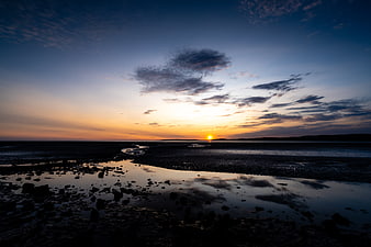Serene Sunset Over Rocky Beach with Sky Reflections