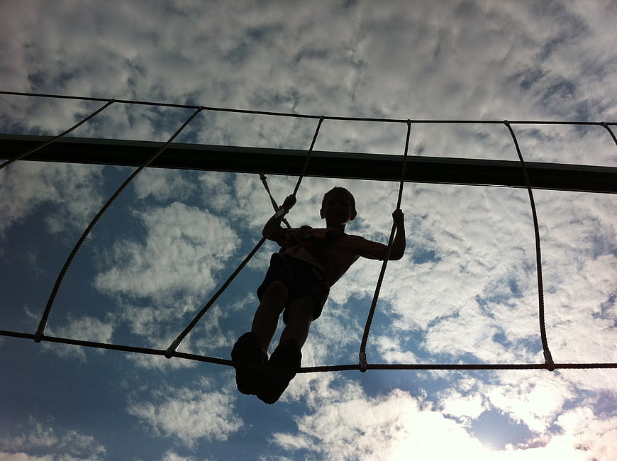 Child Silhouette Climbing Rope Structure Against Cloudy Sky