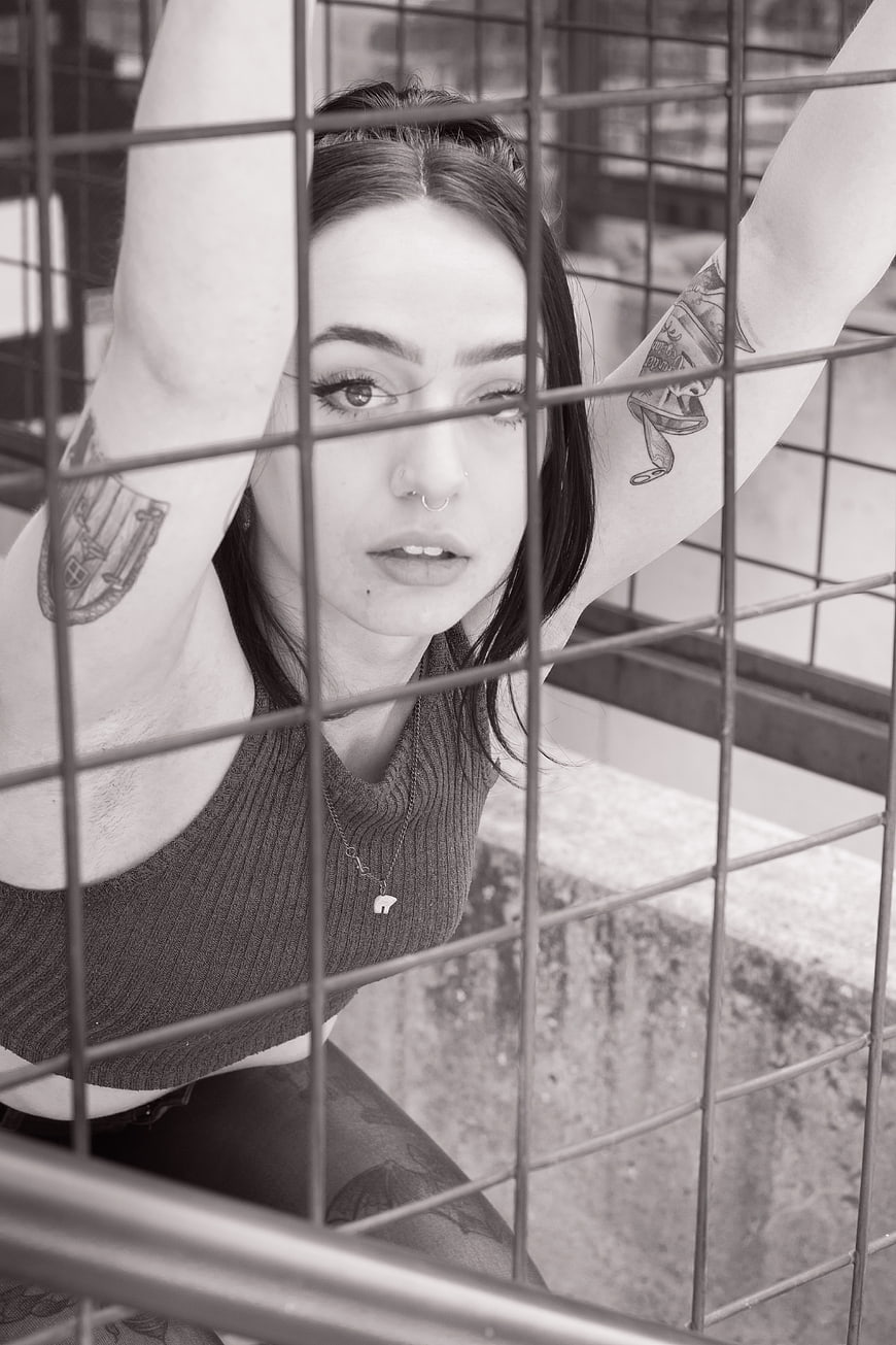 Black and white portrait of tattooed woman behind metal fence