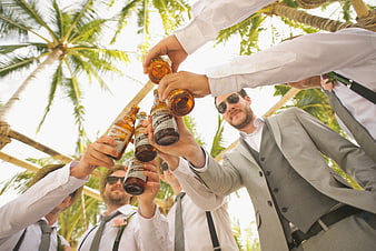 Groomsmen toasting with beer bottles under palm trees