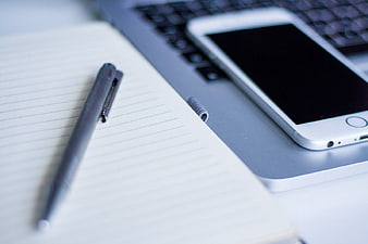White smartphone on laptop with notebook and pen