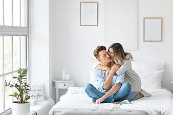 Happy couple embracing and kissing on bed in bright bedroom