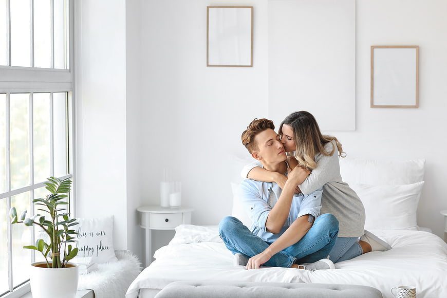 Happy couple embracing and kissing on bed in bright bedroom