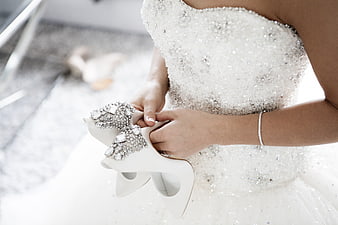 Bride holding jeweled white wedding shoes