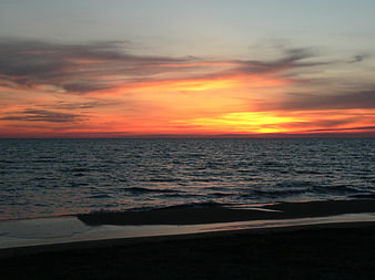 Vibrant orange sunset over calm ocean waves and dark beach