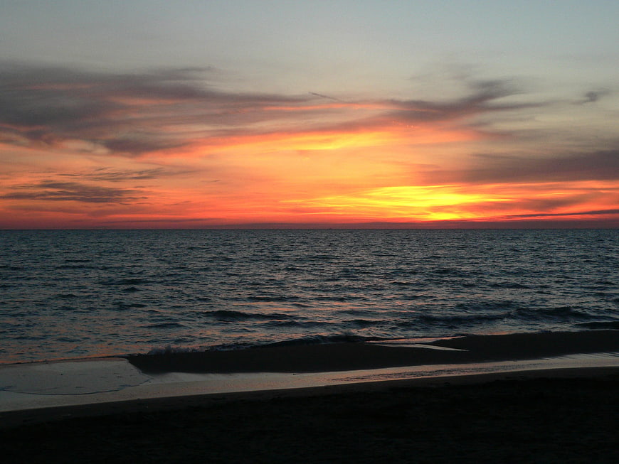 Vibrant orange sunset over calm ocean waves and dark beach