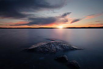 Serene Sunset Over Calm Ocean with Silhouetted Rock