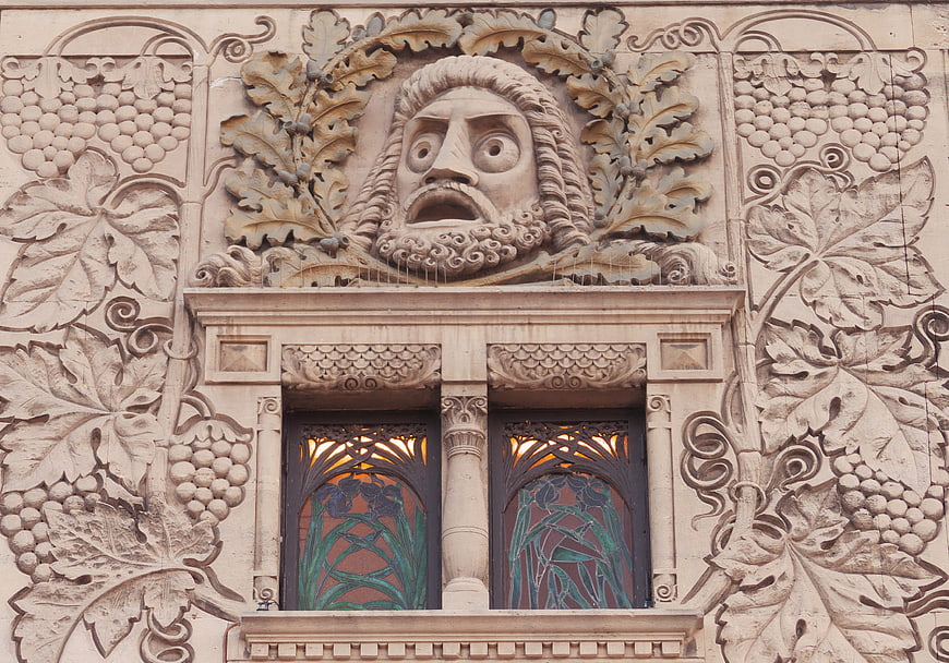 Art Nouveau stone facade with grotesque face and grape motifs