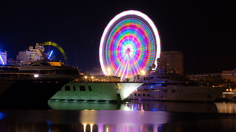 Luxury Yachts Docked at Night with Colorful Ferris Wheel