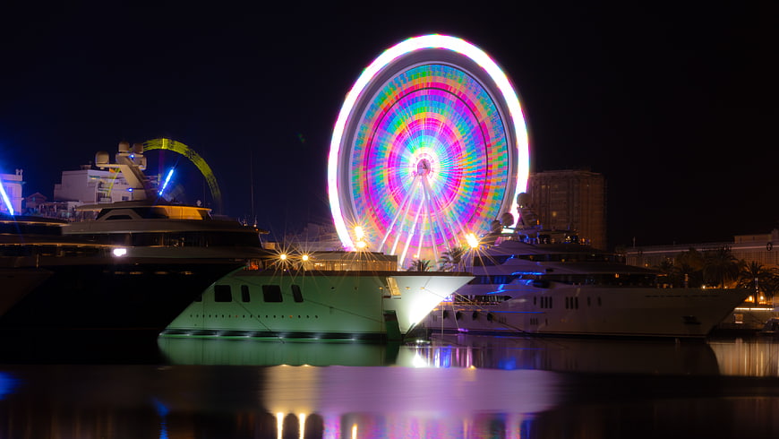 Luxury Yachts Docked at Night with Colorful Ferris Wheel