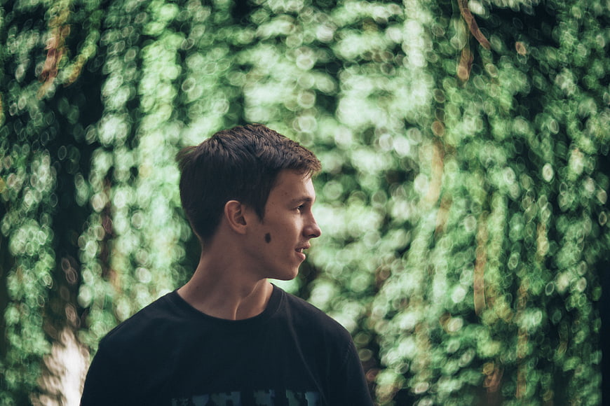 Young man in profile against blurred green forest background