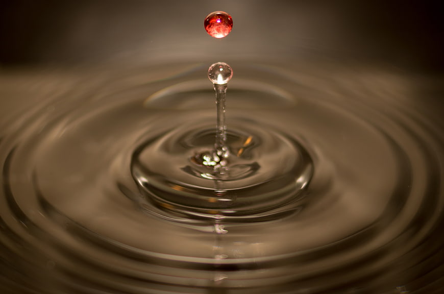Red liquid drop splashing into water with ripples