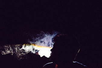 Silhouette of man exhaling smoke against dark background
