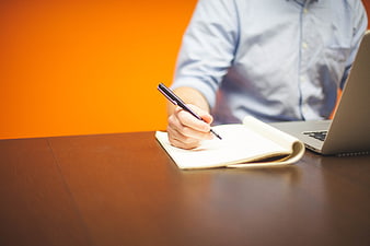 Businessman Writing in Notebook at Desk with Laptop