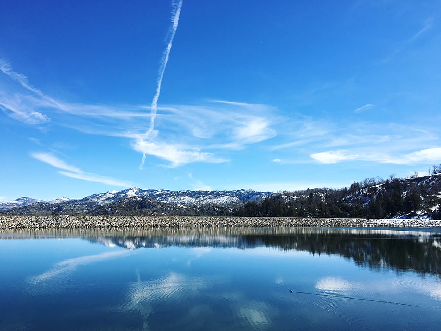 Serene winter lake with snow-capped mountains and blue sky reflection