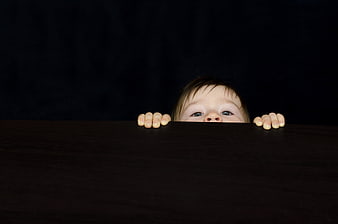 Curious baby peeking over dark wooden table