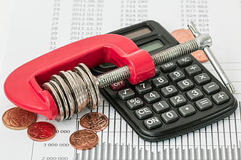Red clamp squeezing coins on calculator for budgeting