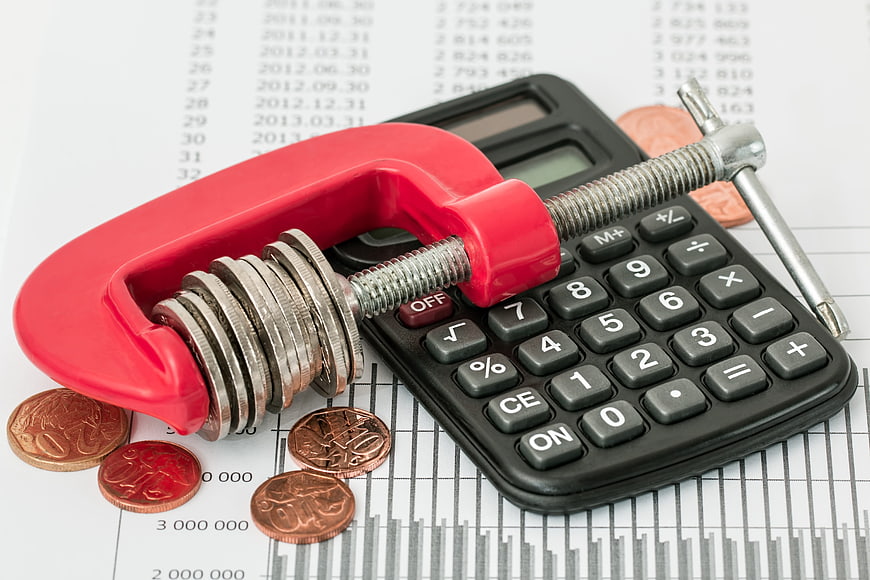 Red clamp squeezing coins on calculator for budgeting