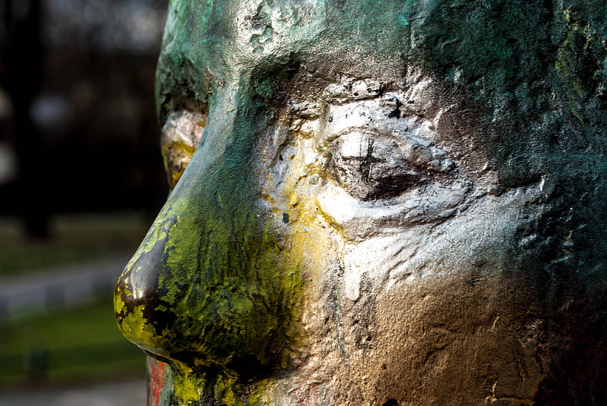 Close-up of weathered bronze statue face with graffiti