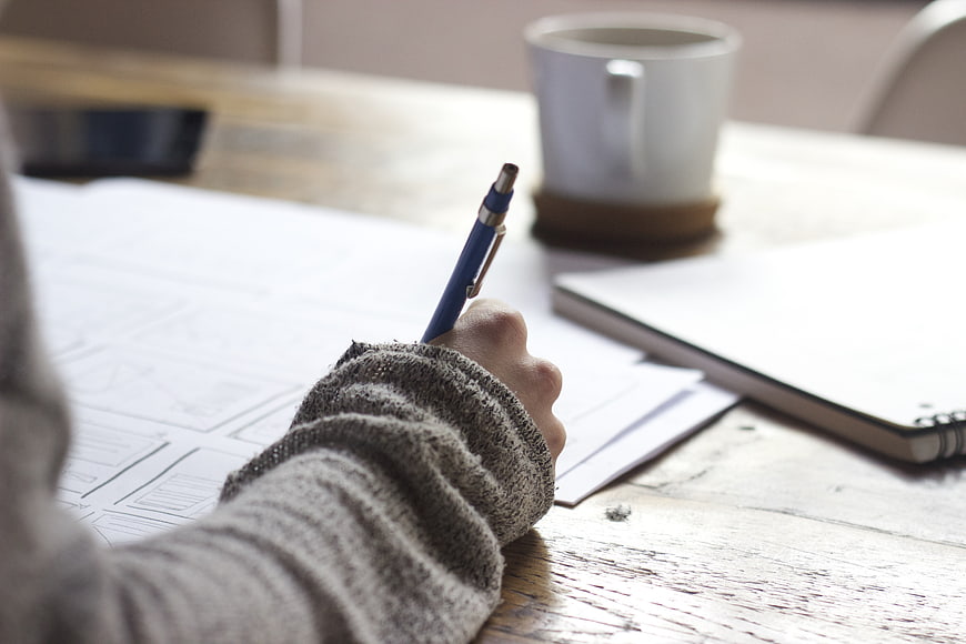 Hand sketching wireframes on desk with coffee and notebook
