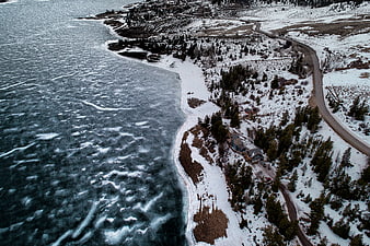 Aerial view of frozen lake shoreline with winding road and snow