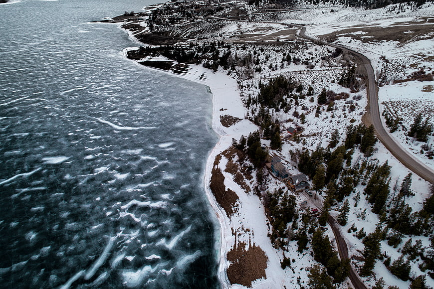 Aerial view of frozen lake shoreline with winding road and snow
